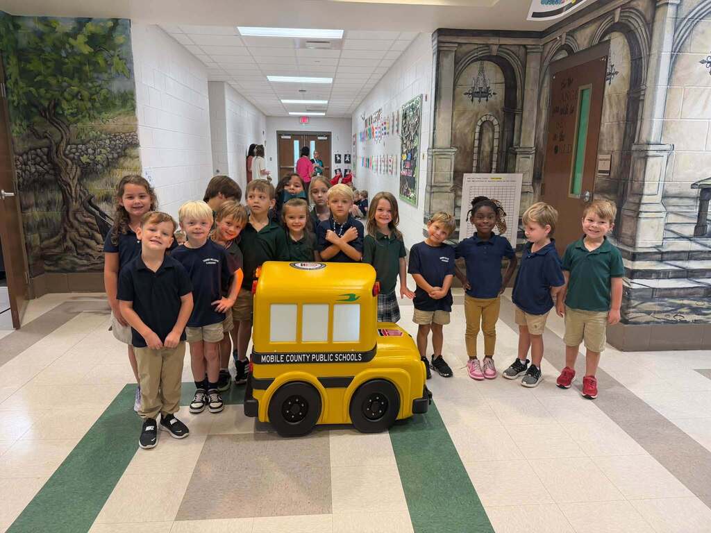 Students at Tanner Williams Elementary smiling beside "Buster" the minature school bus. 