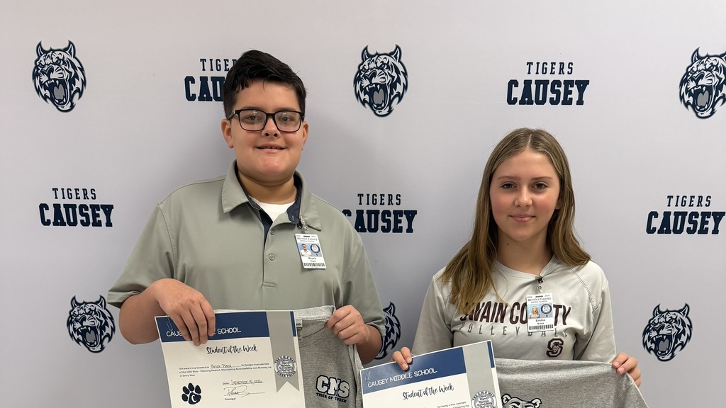 Two students, a boy and a girl, stand with certificates in a room with a wall design.