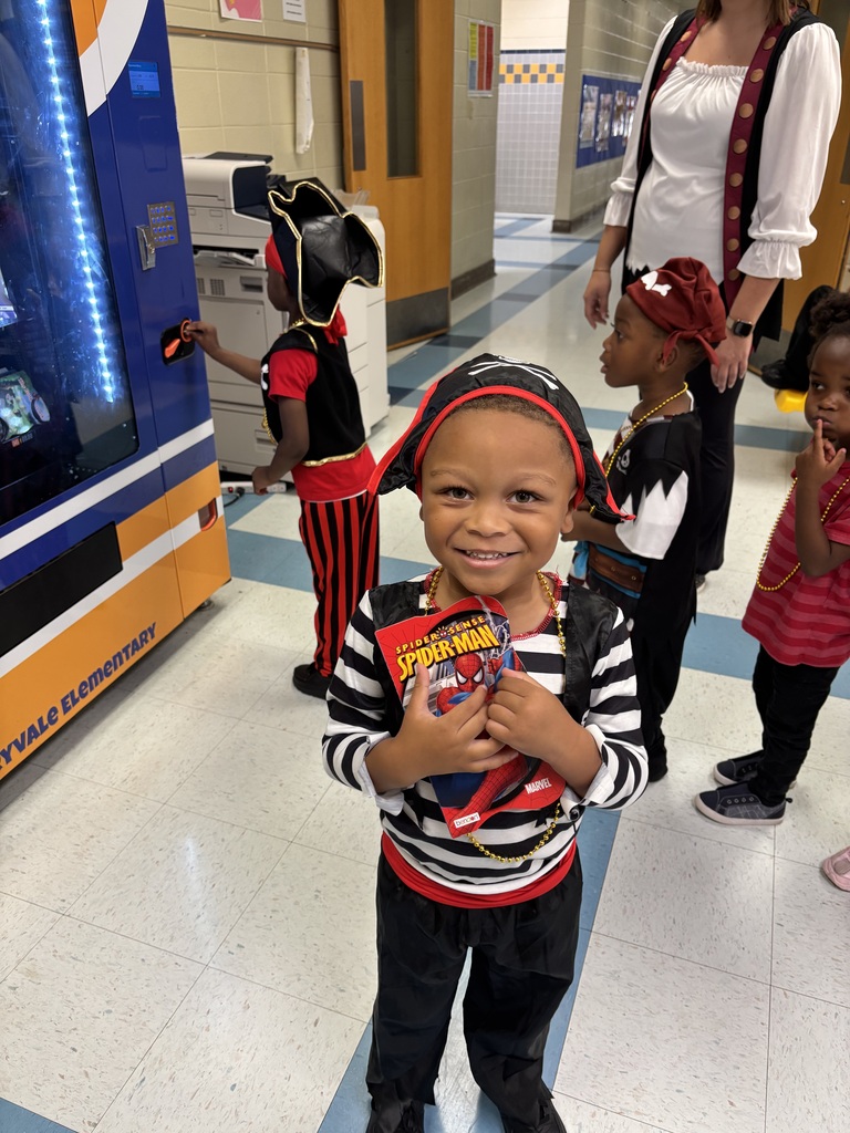 Child in a striped shirt with a red pirate hat smiles at the camera. Other children in pirate costumes stand behind.