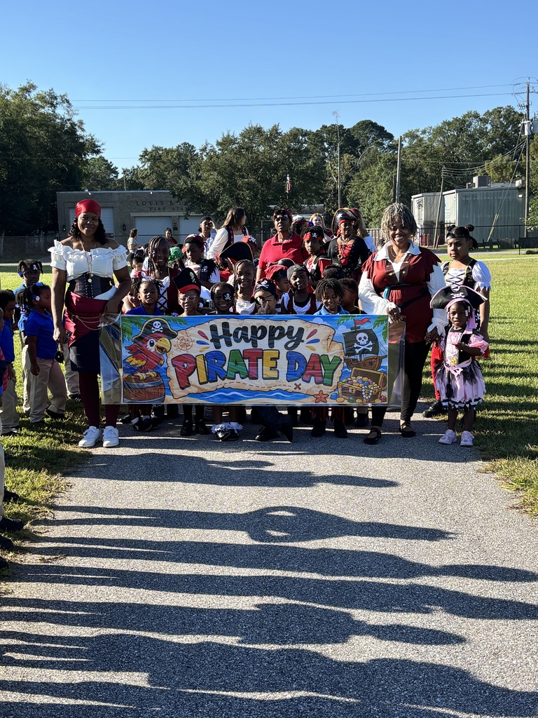 A group of people dressed in costumes with a banner reading "Happy Pirate Day" on a paved path.