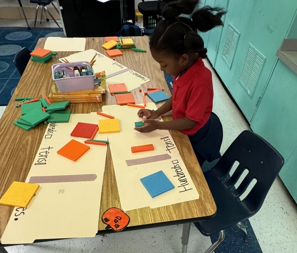 A child arranges various colored shapes on a table, with several papers attached and labeled.