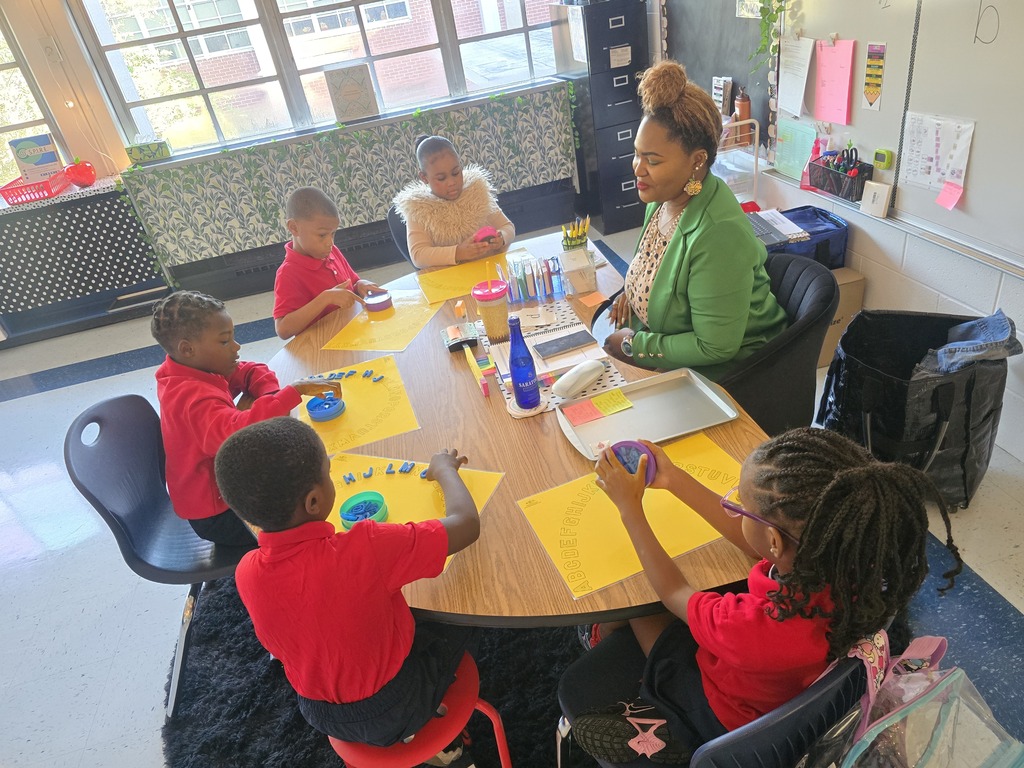 Five children and an adult sit around a table with yellow papers and supplies.