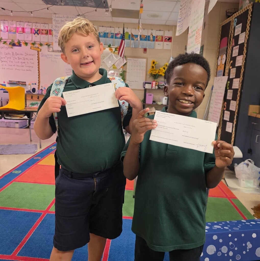 Two smiling students holding fake paychecks