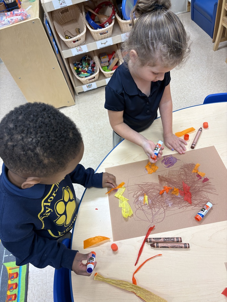 Two children work on an art project with markers and construction paper on a table.