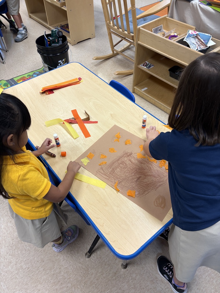 Two children work on an art project at a table with orange paper and craft materials.