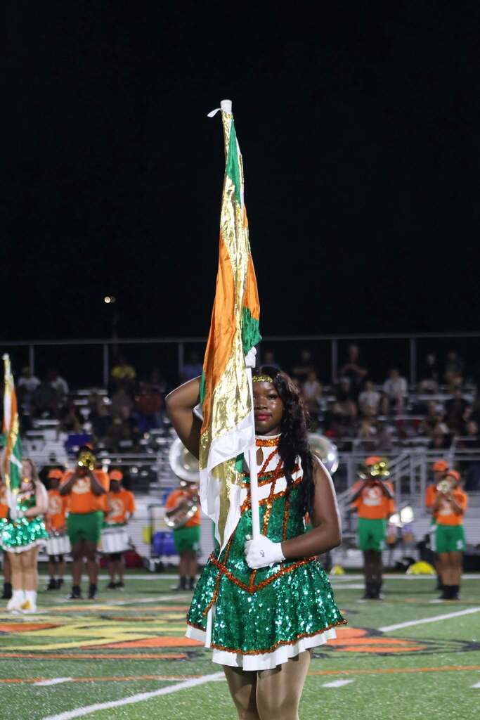 A flag corps member holding a flag in front of a marching band