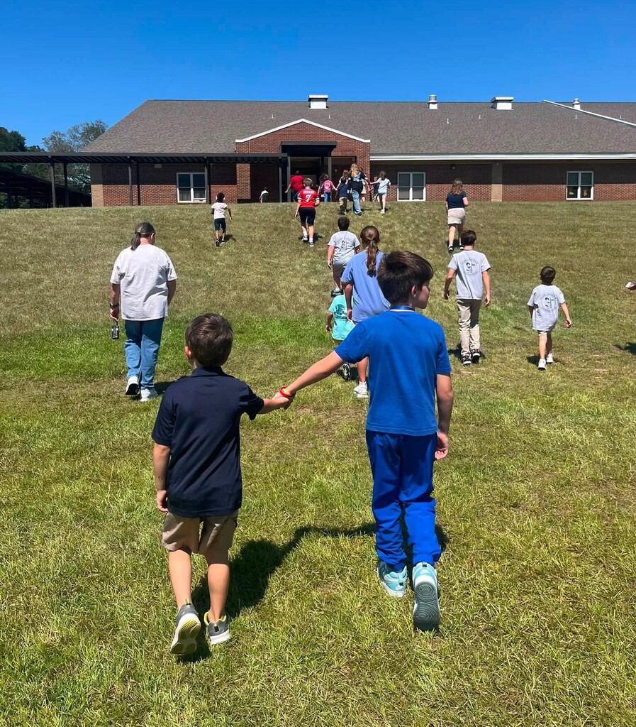 A fifth grader and kindergartener hold hands as they join other classmates in walking toward a school building