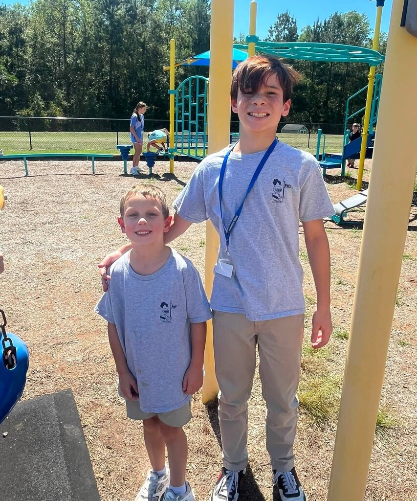 A fifth grader stands with his arm on the shoulder of a kindergartener