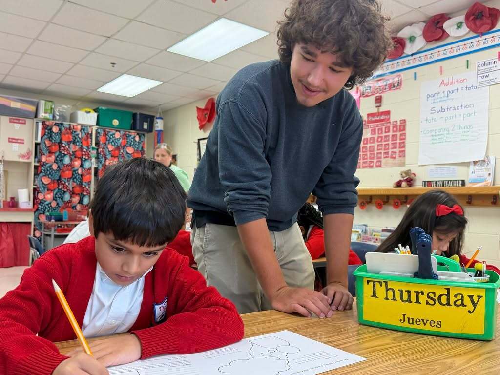 A high school student watches an elementary student writing