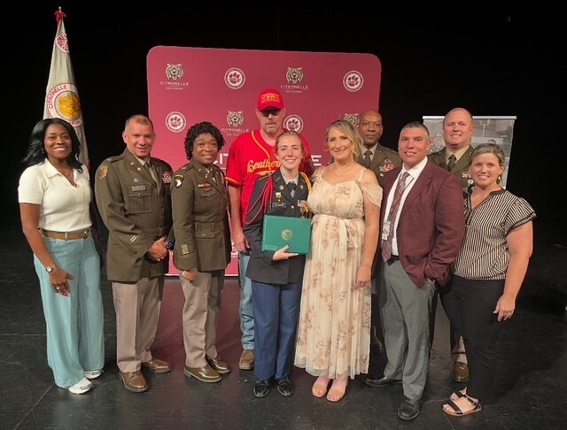 A JROTC cadet stands with parents, instructors and school officials