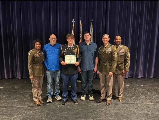 A JROTC cadet stands with instructors and parents