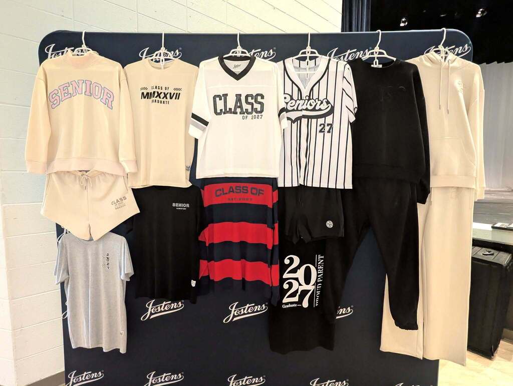 Various clothing items hang on hangers on a black wall. Items include a cream-colored sweatshirt, a black and white striped shirt, and a red and white striped shirt.