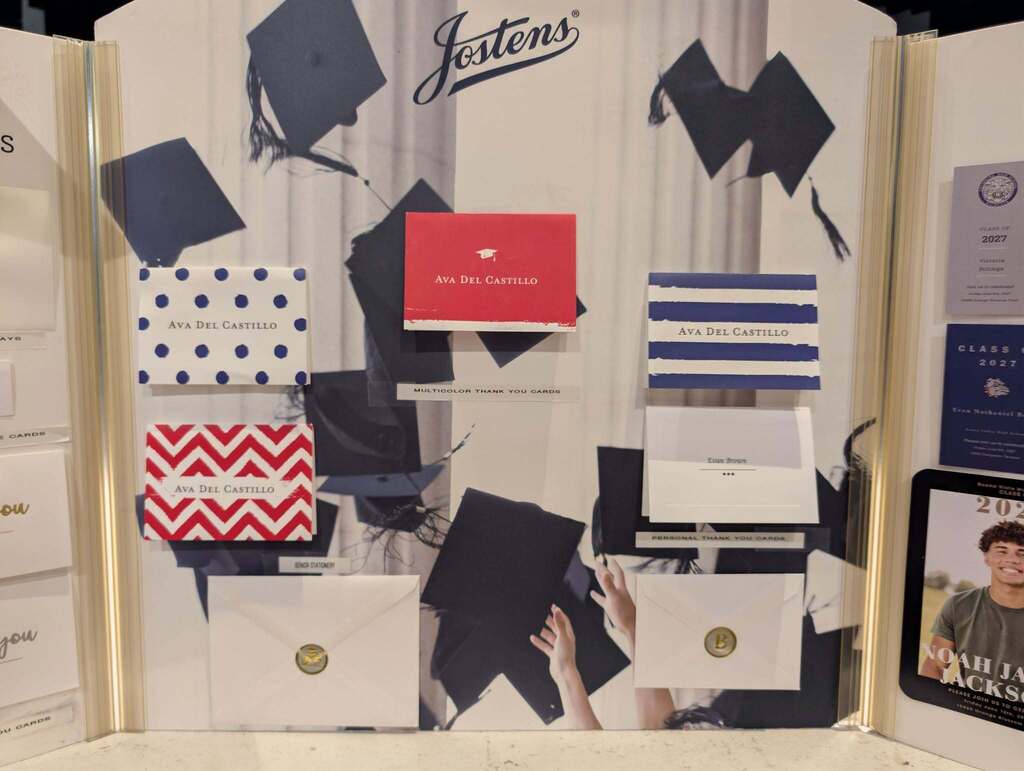 Display of various colored and designed invitations, some with "Jestions" text, arranged on a wall with graduation caps.
