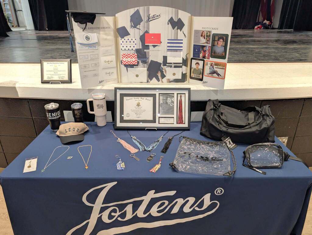 Display at a table with Jostens products, including graduation caps, certificates, and bags, on a blue tablecloth.