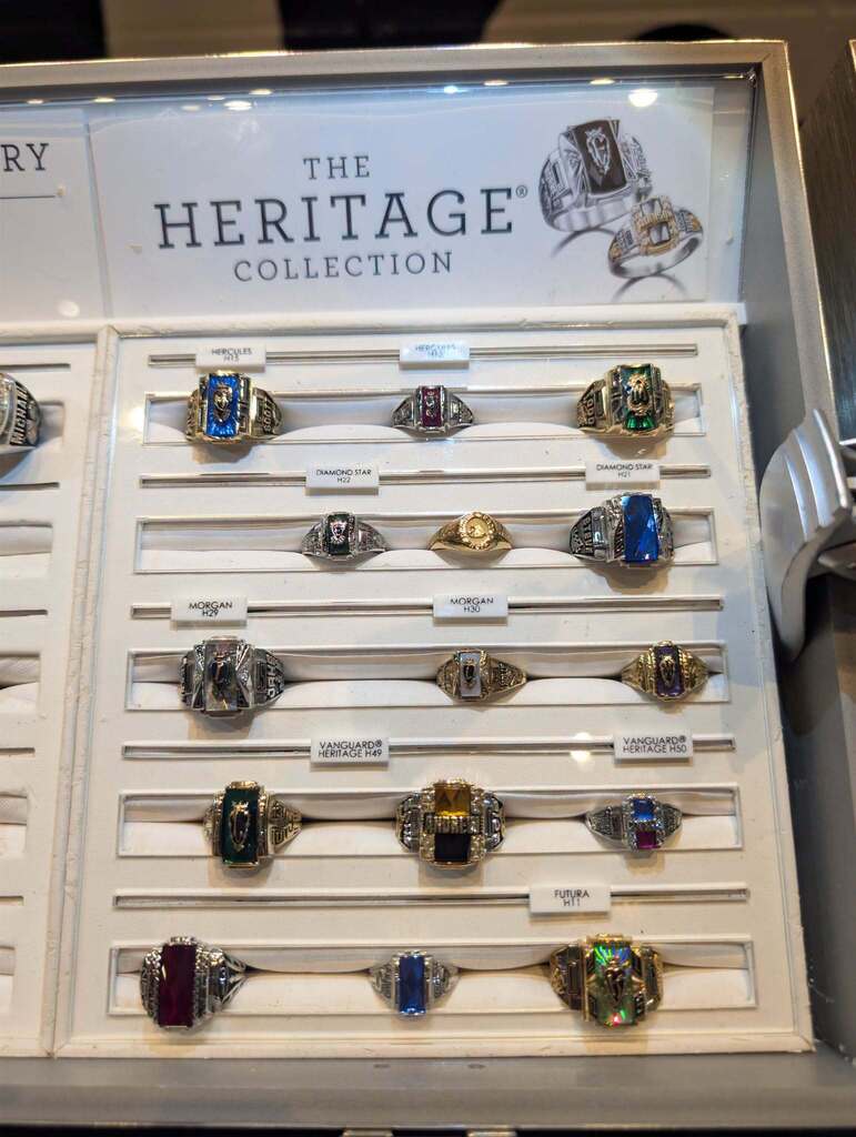 Display of various colorful rings in a white box with labels. A sign above reads "The Heritage Collection".