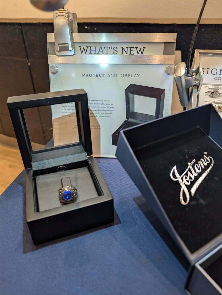 Two jewelry display boxes, one with a blue ring and the other with "Jetten's" logo. An open sign reads "What's New".