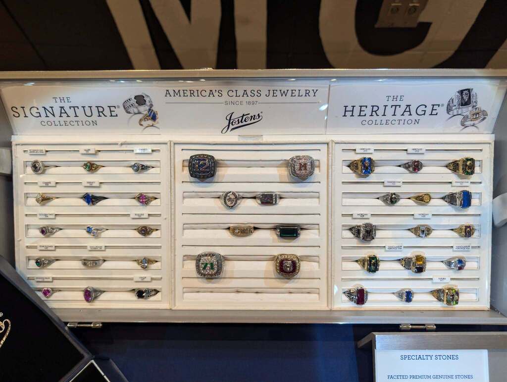 Display case with multiple rows of rings, labeled "The Signature Collection" and "The Heritage Collection" with white background.