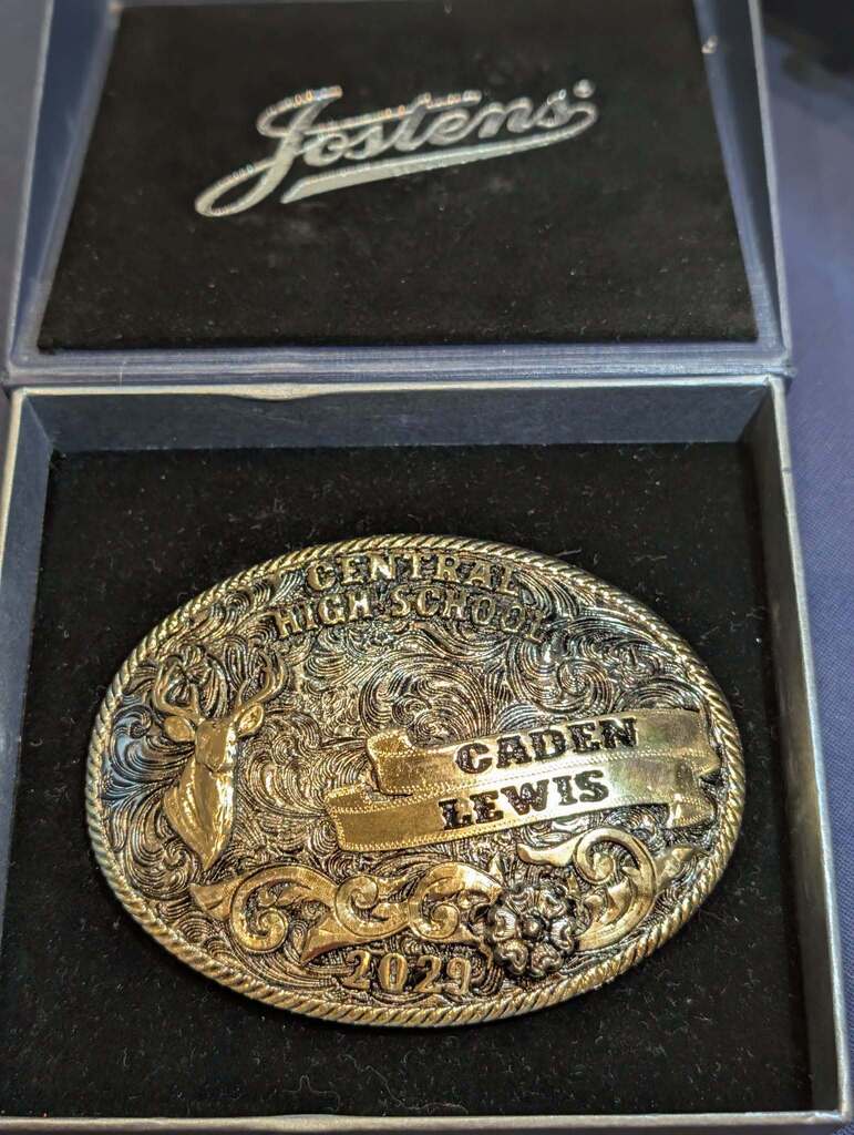 A gold belt buckle inside a box. The buckle reads "Central High School" and "Caden Lewis 2019" with a deer design.