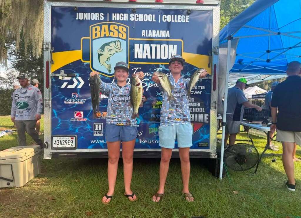 Two individuals, one in shorts and the other in a skirt, pose with fish in front of a truck.