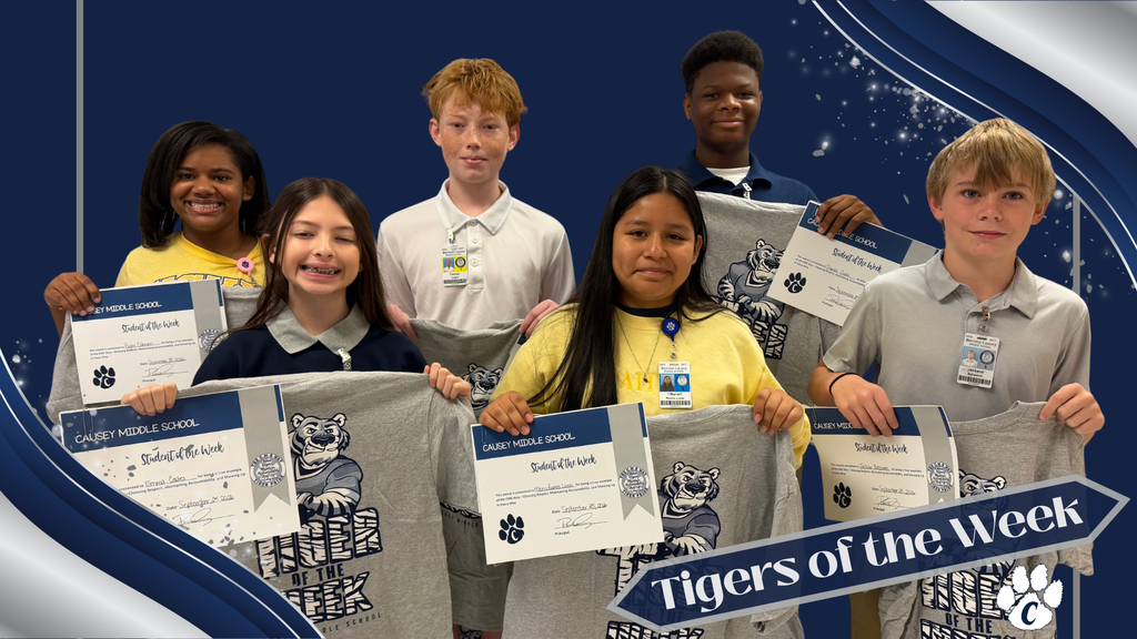 A group of children hold up certificates, wearing blue shirts, and gray T-shirts. They are posing.
