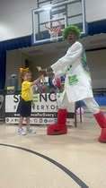 A person in a costume and a child in a yellow shirt interact indoors, possibly at a school event.