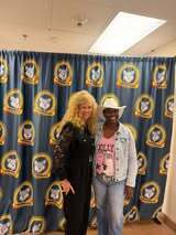 Two women stand side by side in front of a blue curtain with yellow and white patterns.