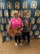 Woman with short blond hair in pink top holding a guitar stands next to a man in gray shirt.