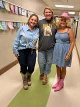 Three adults in a hallway, one in a denim dress, another in a cowboy hat, and a third in a blue shirt.
