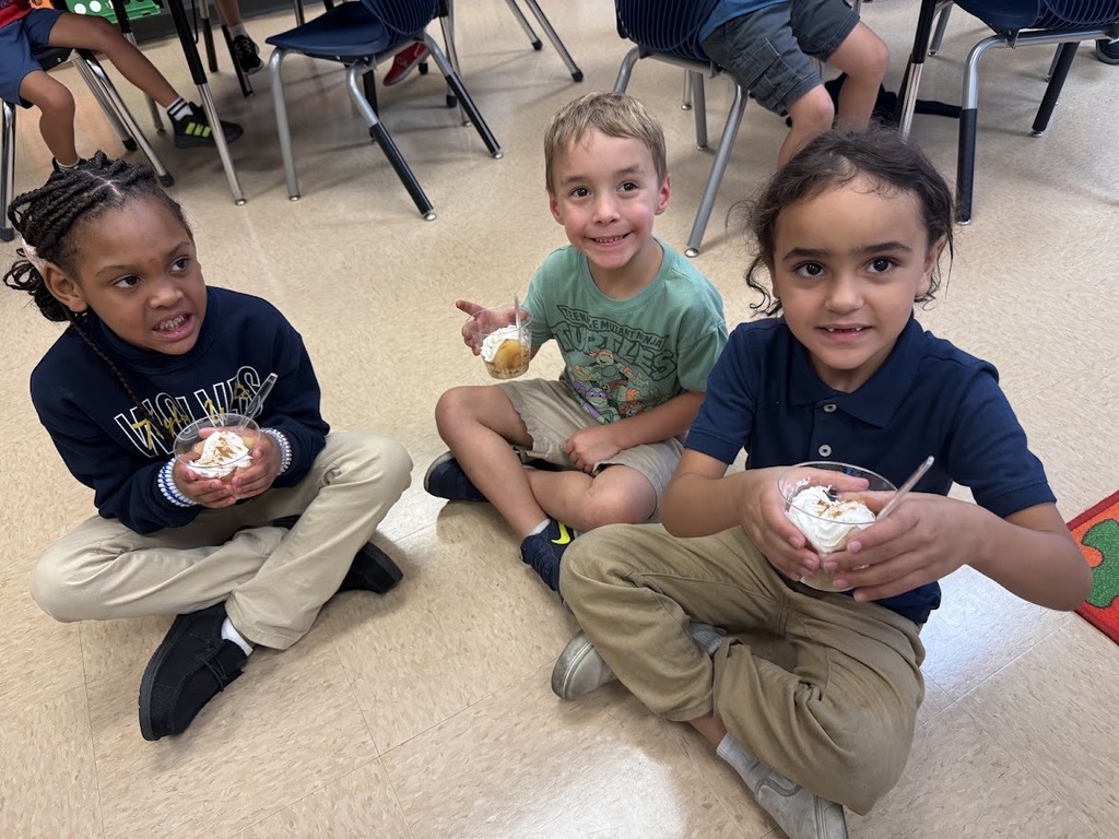 Four young children sit on the floor in a classroom, each holding a treat in a cup.