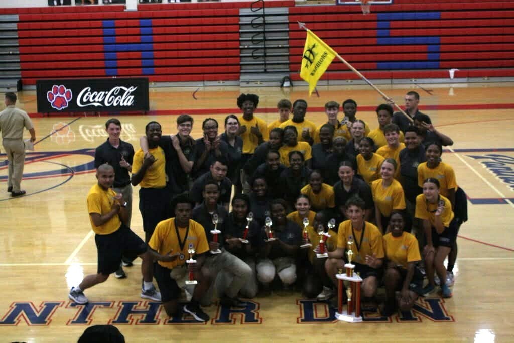 A group of JROTC cadets, with trophies and a yellow flag