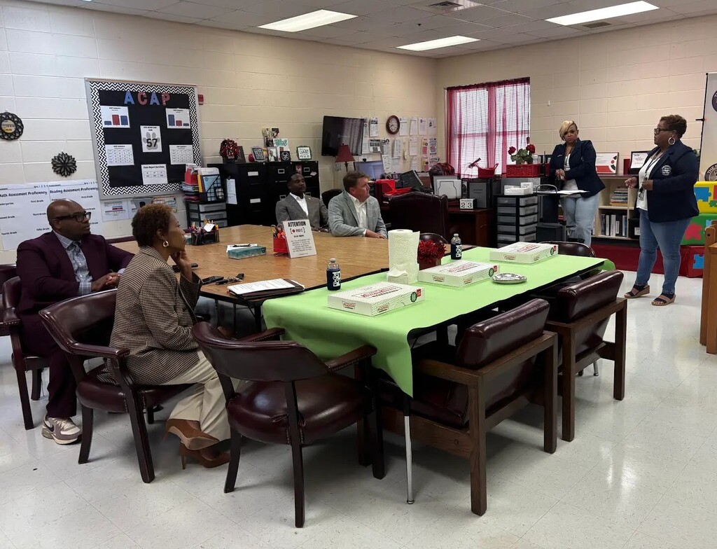 Two educators talking to four council people seated at a table