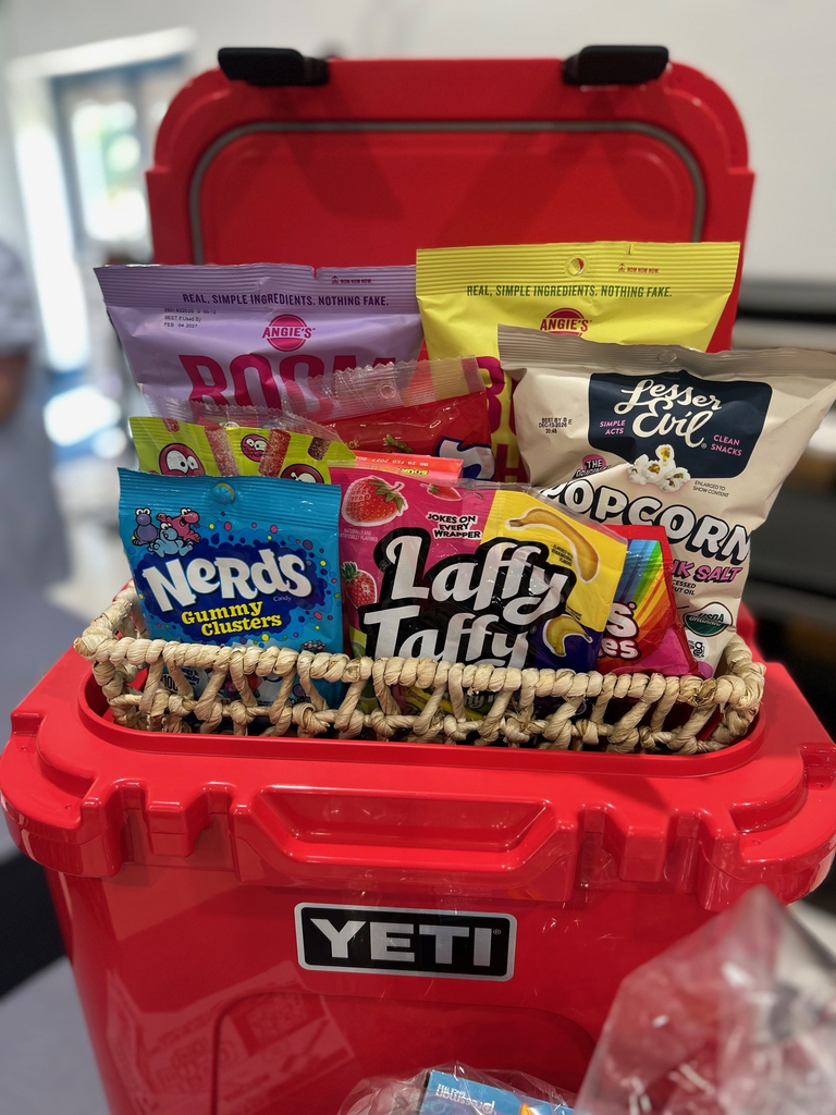 A red cooler box filled with colorful snacks, including Nerds, Laffy Taffy, popcorn, and chips. The box is branded with the word "YETI."