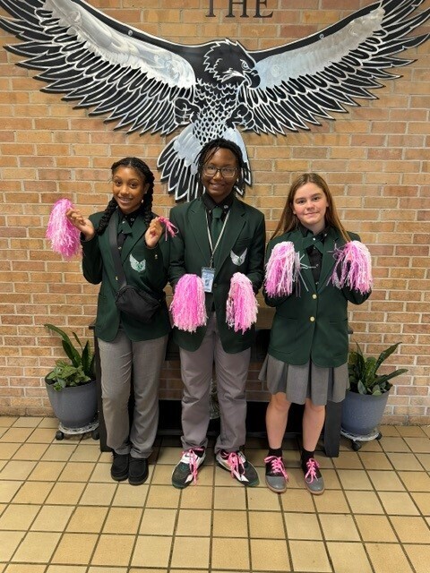 picture of 3 9th graders holding pink pompoms and pink shoelaces