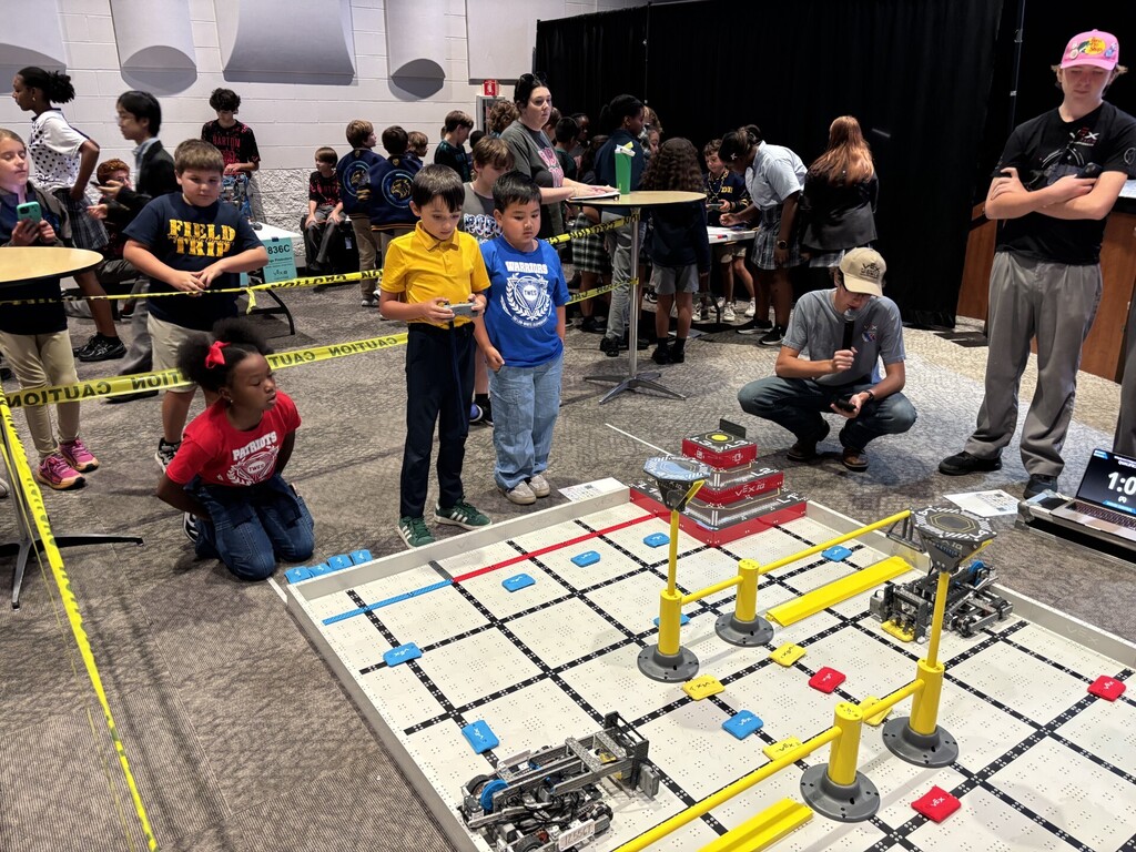 A group of kids and adults are gathered around a table with a robot competition course.