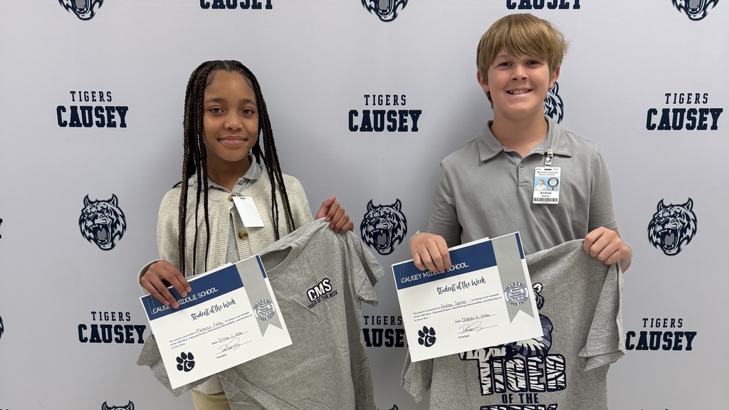 Two children stand with certificates, one holding gray shirts, the other holding blue shirts, against a black and white background.