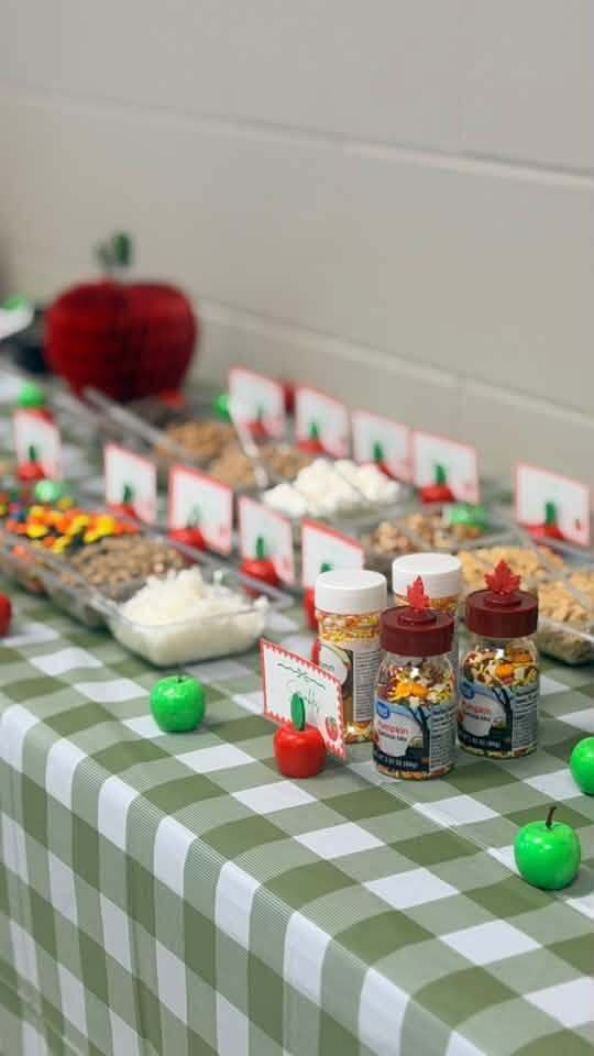 A table covered with a green-and-white gingham tablecloth displays a variety of snacks in clear containers.