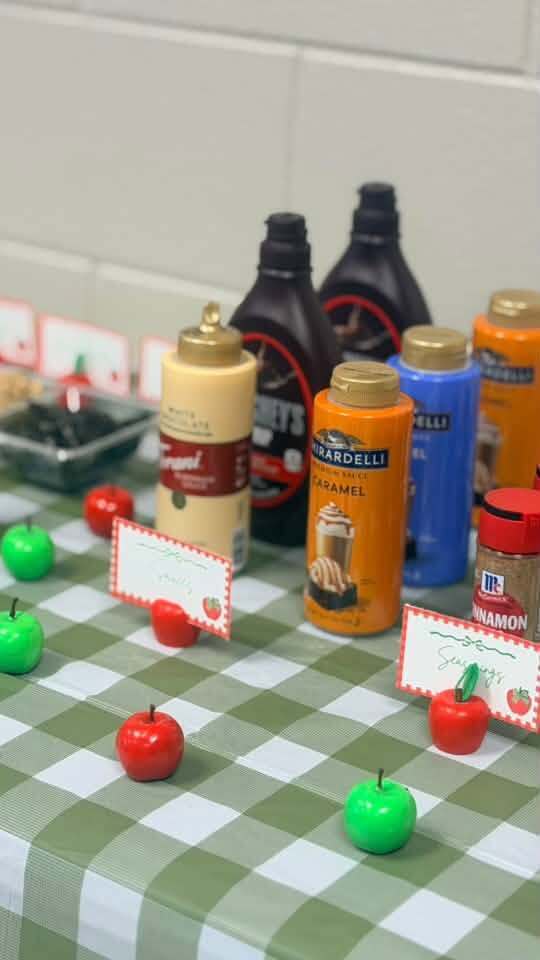 Bottles of syrup and apple-shaped containers on a table with a green and white checkered tablecloth.