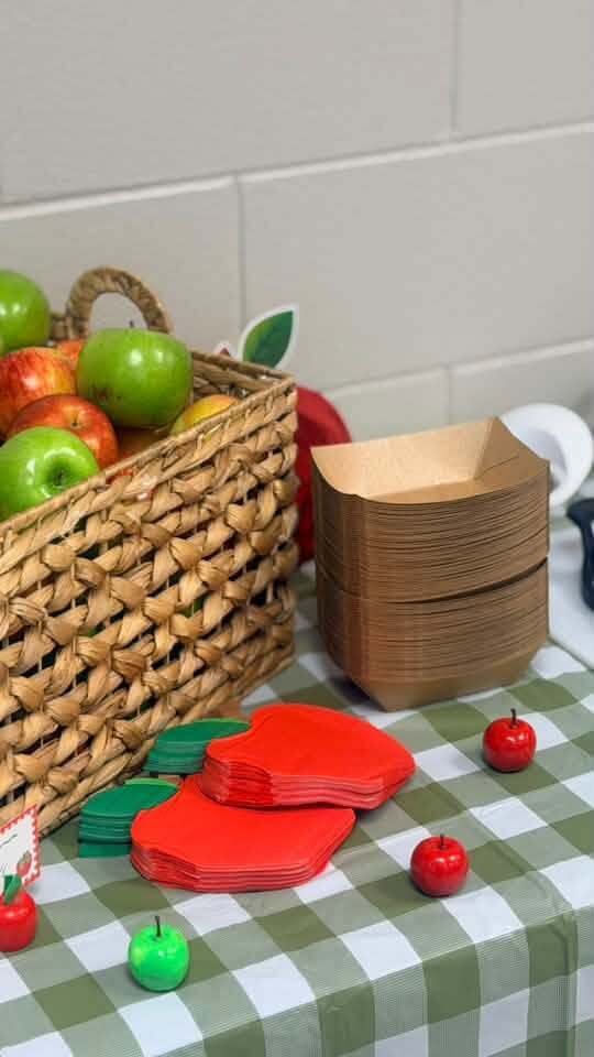 A basket filled with green apples rests on a table covered in a green and white gingham tablecloth.