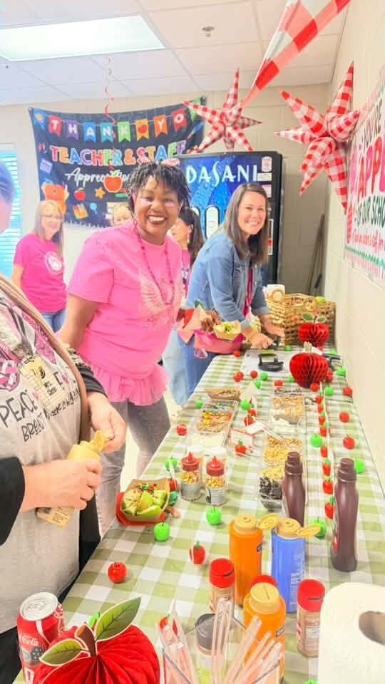 Three women at a table with food. A banner reads "Thank You Teachers & Staff".