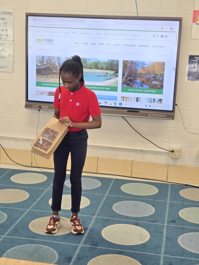 A student holds a paper bag while standing in front of a large screen in a classroom.