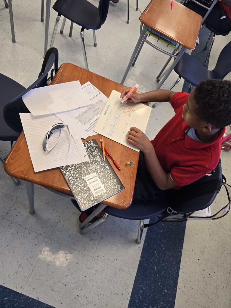 A boy writes on a piece of paper at a desk, surrounded by school supplies.