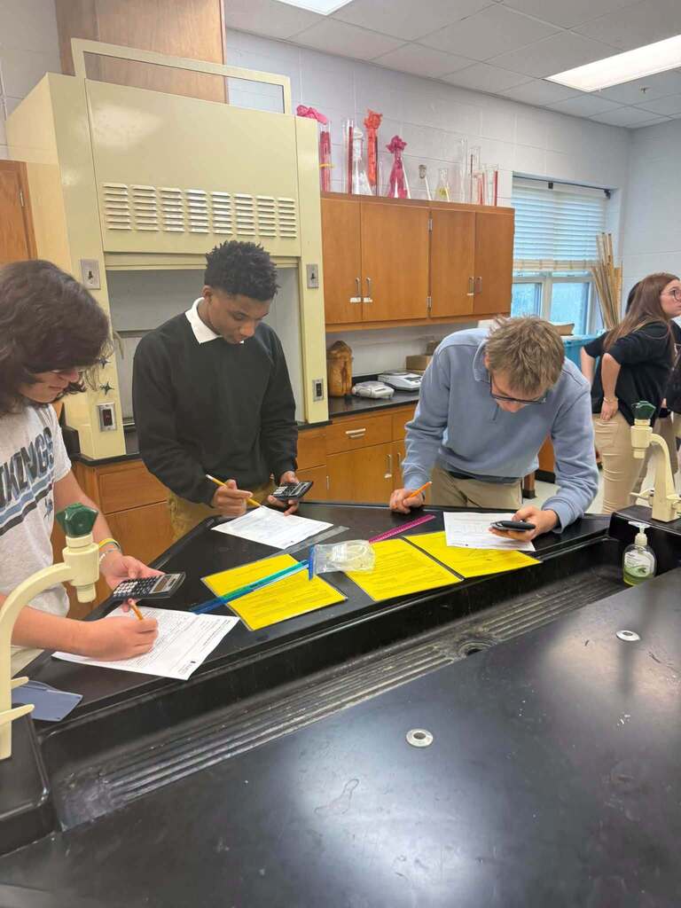 Four people in a science lab, working on a table with papers and a microscope.