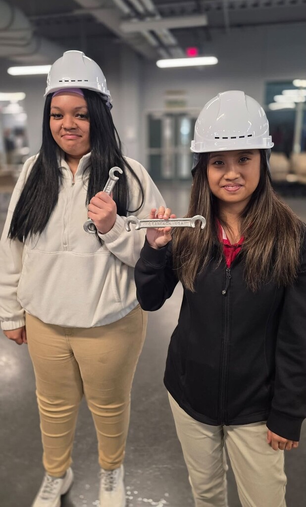 Two girls wearing hardhats and holding wrenches