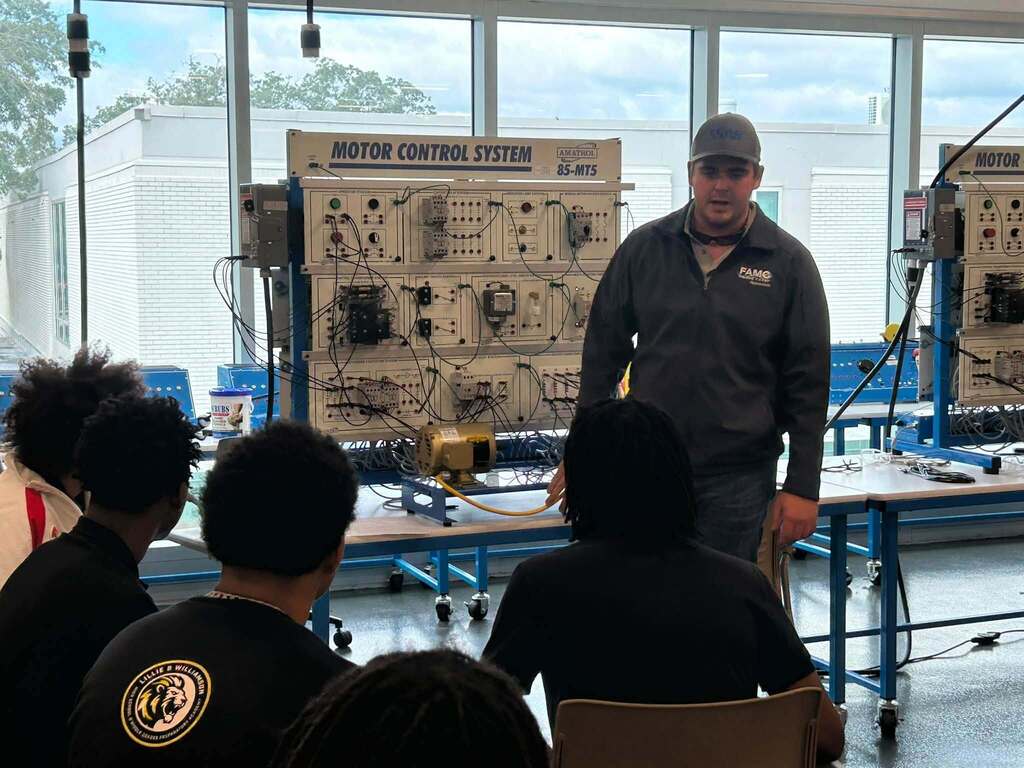 An instructor talks to students in front of a board with wiring