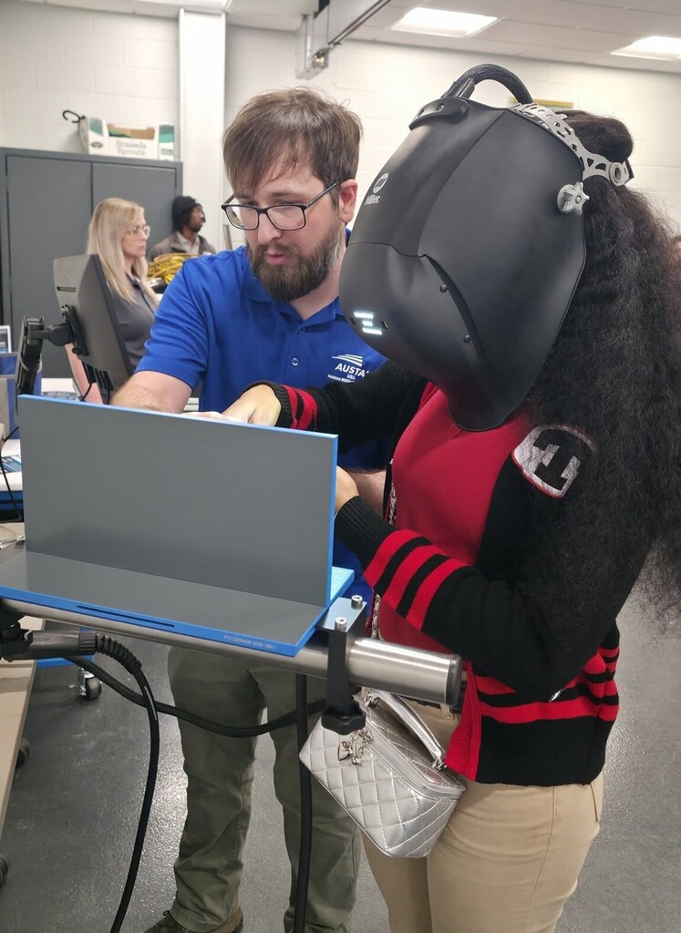 An instructor stands with a student in a welding mask
