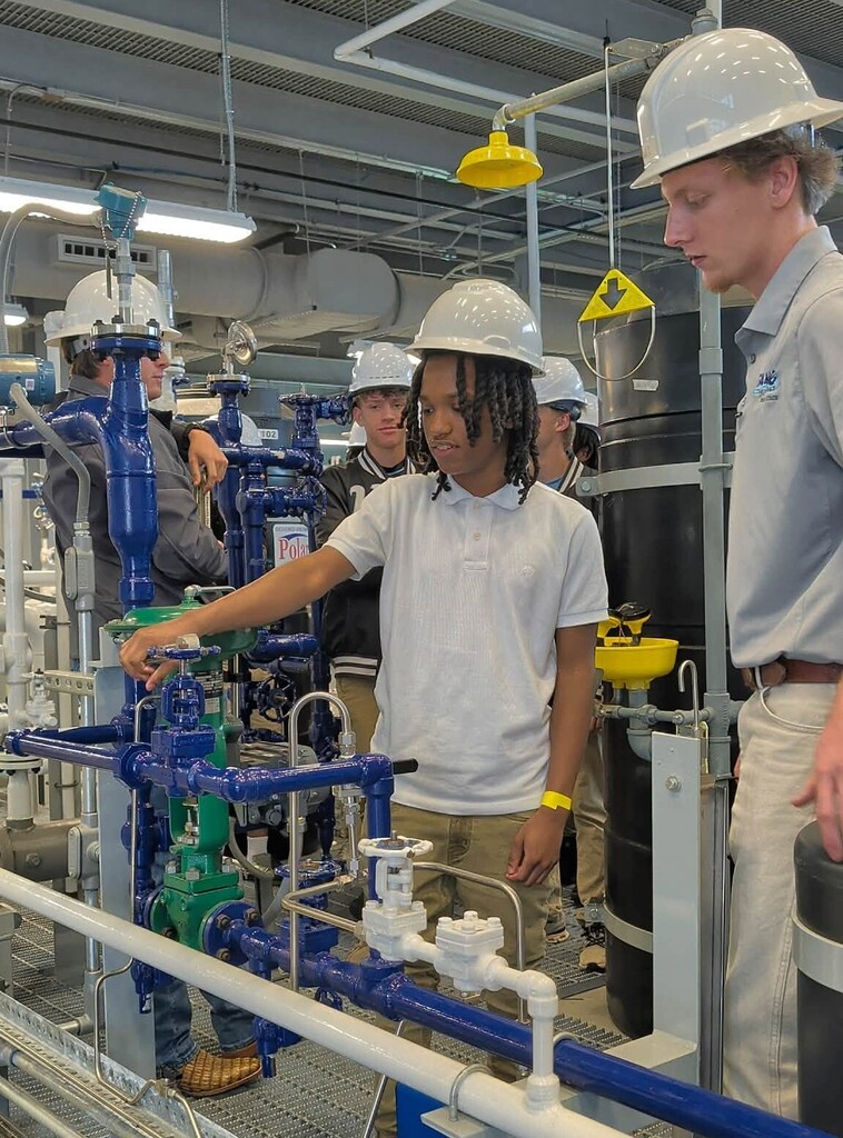 A student in a hardhat turns a valve over some pipes