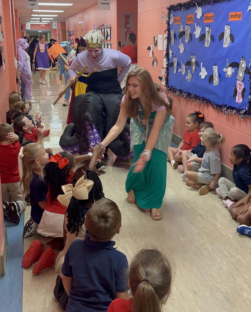 Two teachers dressed as Disney-themed characters shake hands with students in a hallway