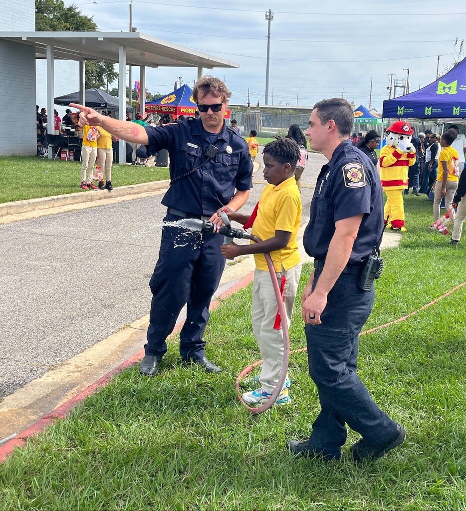 Two firefighters show a student how to use a fire hose