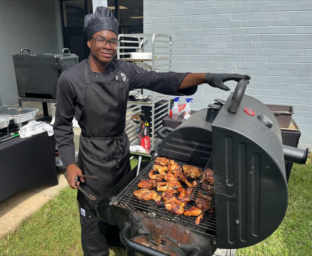 A student stands at a grill full of chicken