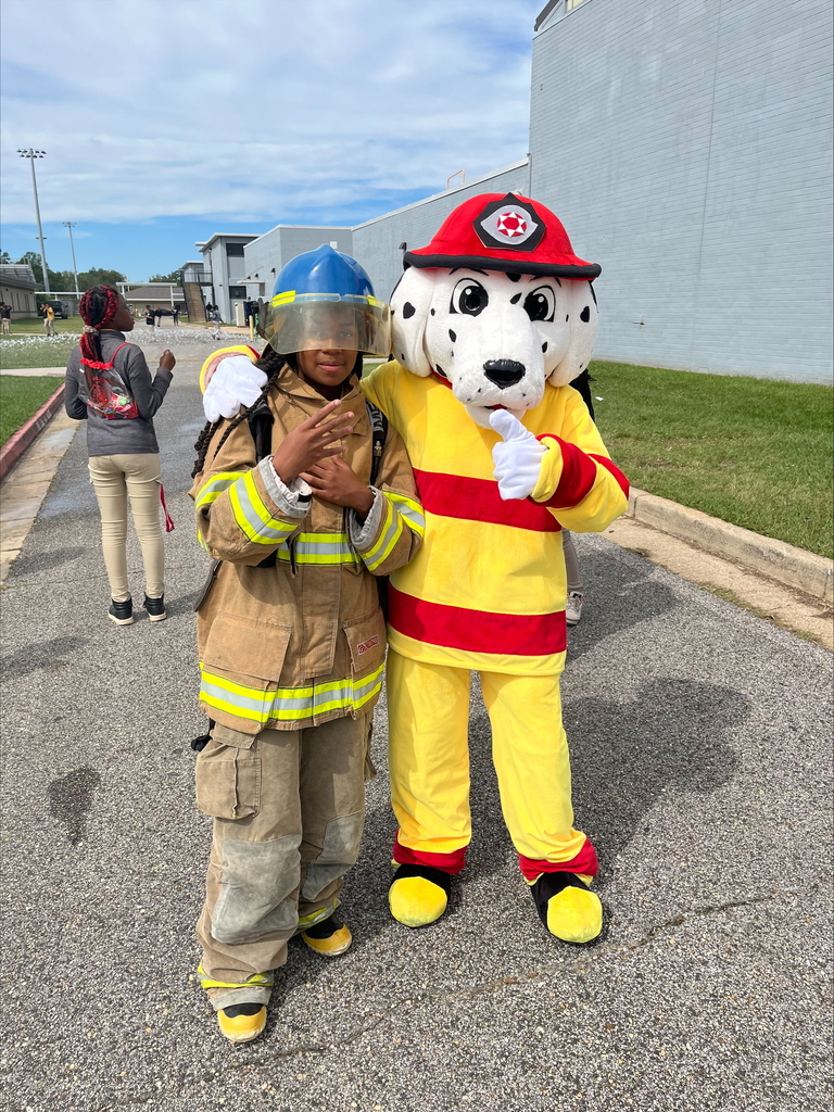 A fire dog mascot stands with a student wearing firefighter gear